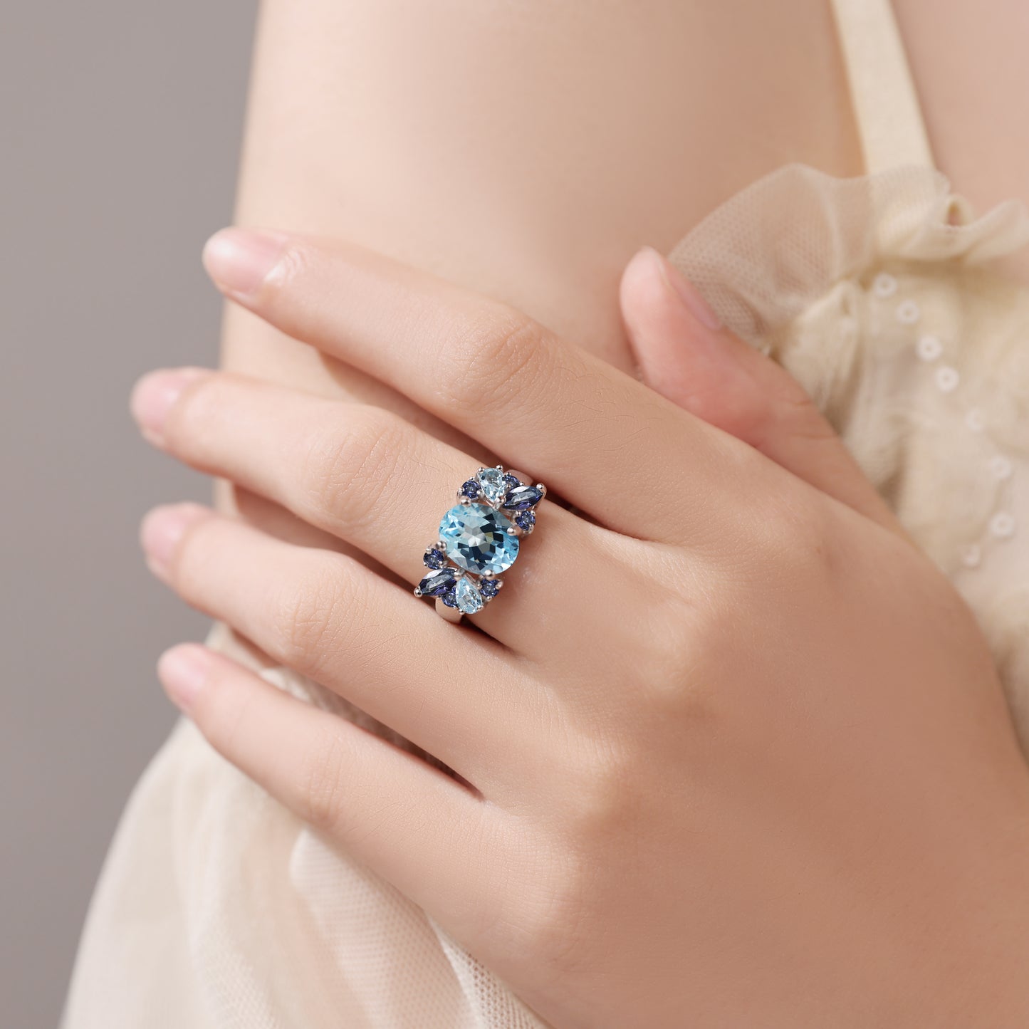 Close-up of a hand wearing a blue topaz ring against a neutral background