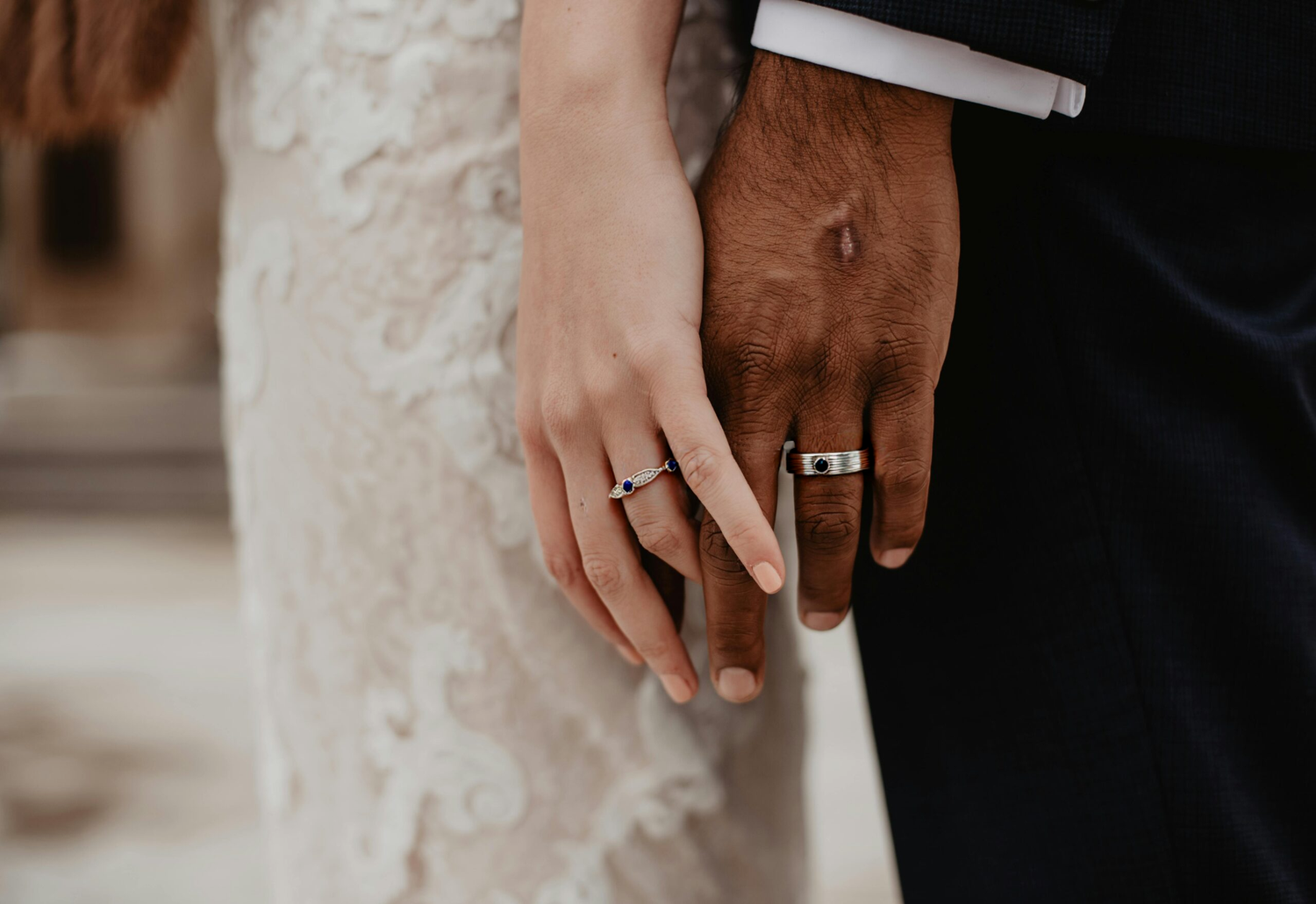 Close-up of hands holding together, wearing wedding rings, with a blurred background.