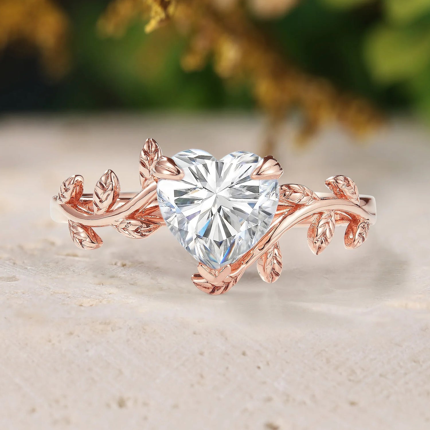 Rose gold ring with heart-shaped diamond on a textured surface with blurred greenery in the background