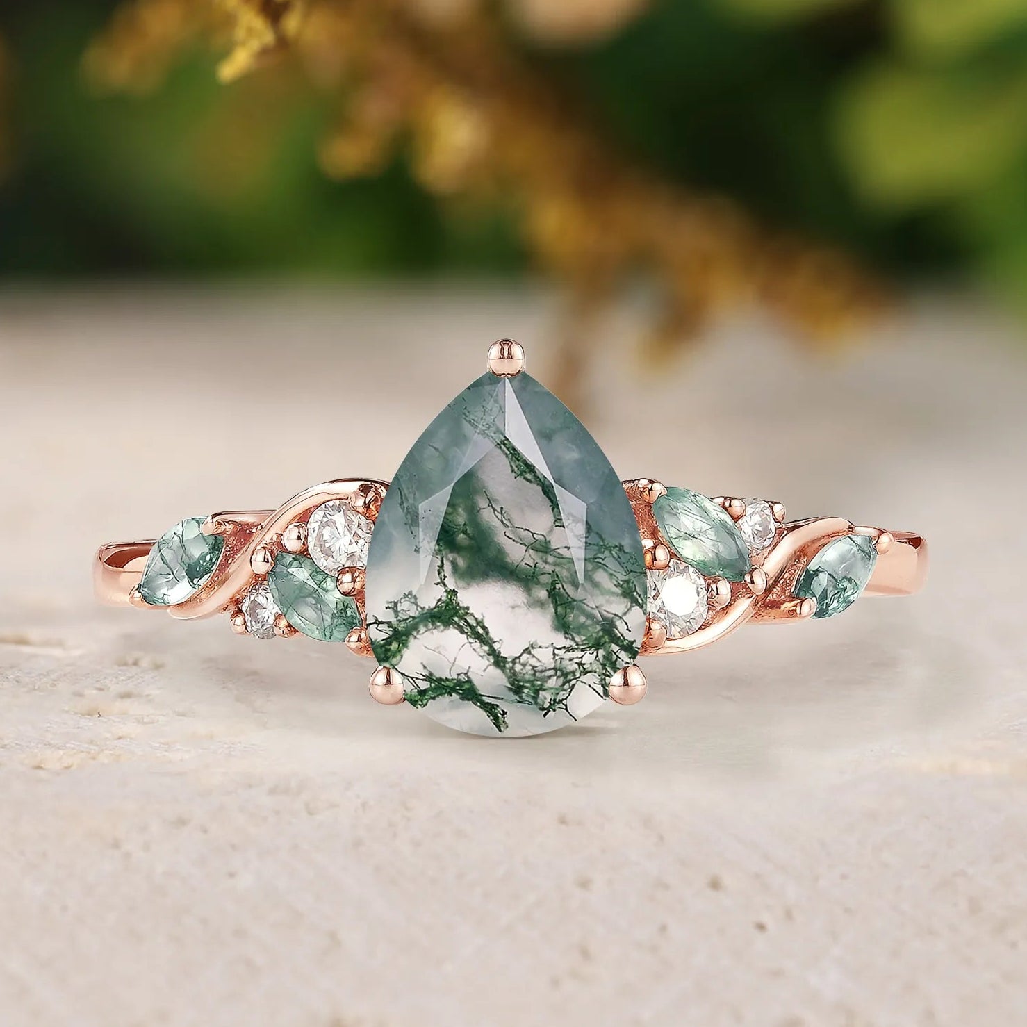 Rose gold ring with a green teardrop-shaped gemstone on a light background