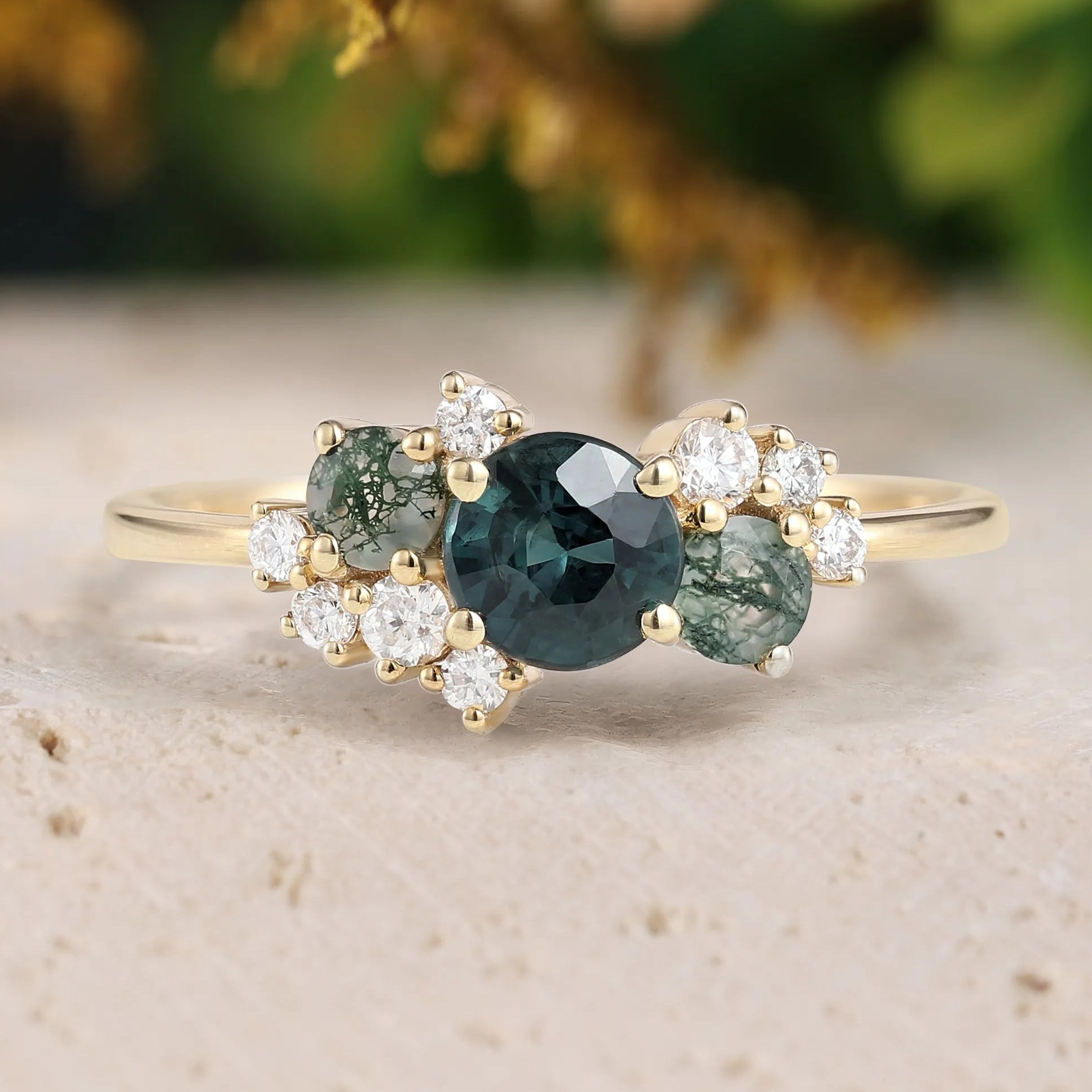 Gold ring with green gemstones and diamonds on a textured surface with blurred natural background