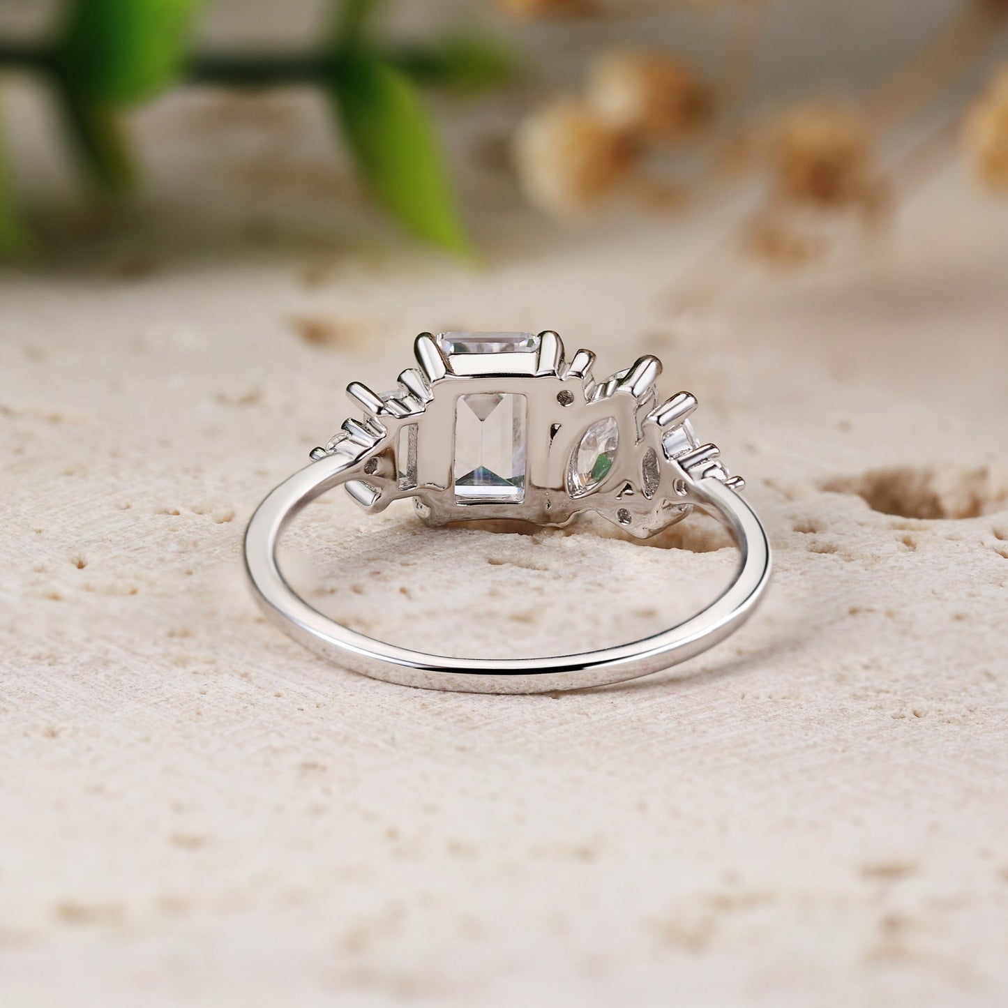 White gold ring with a large diamond on a textured surface with blurred green and brown elements