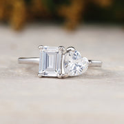 Diamond ring with heart-shaped and emerald-cut stones on a neutral background