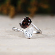 Silver ring with a red gemstone and a clear gemstone on a light surface.