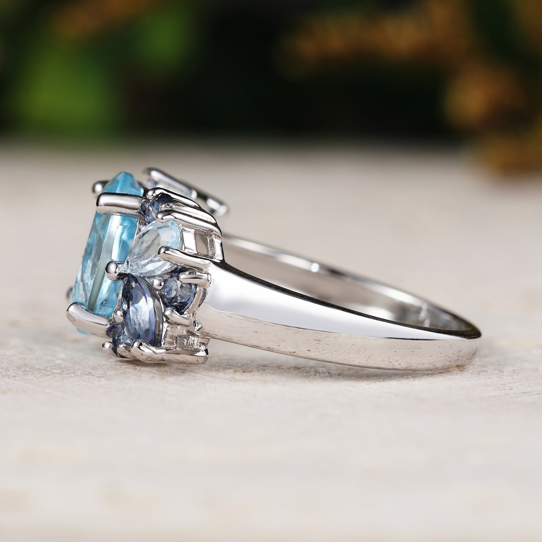 white gold ring with blue topaz on a light surface with blurred greenery in the background