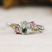 White gold ring with multicolored gemstones natural tourmaline on a light surface with blurred natural background
