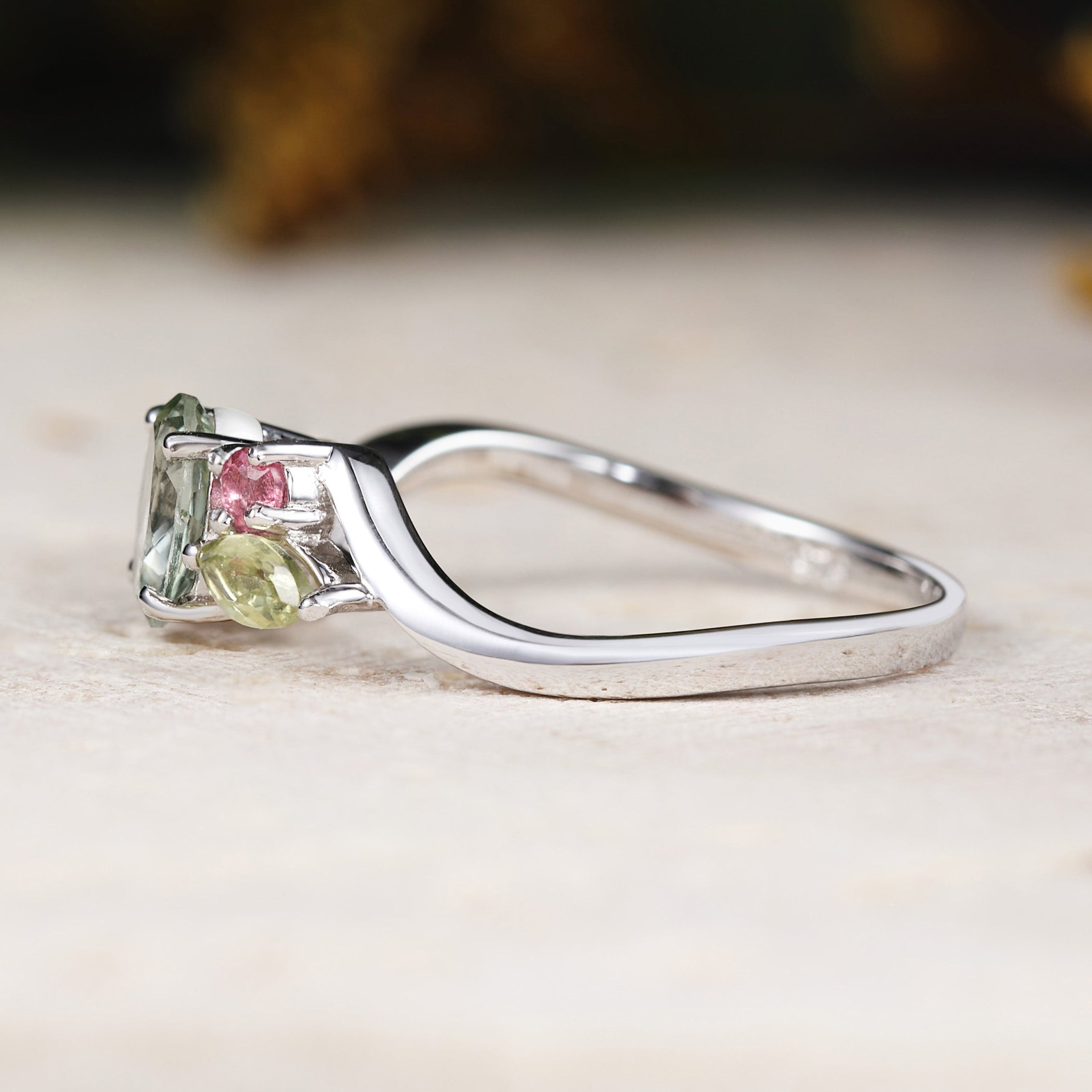 White gold ring with green and pink gemstones on a neutral background