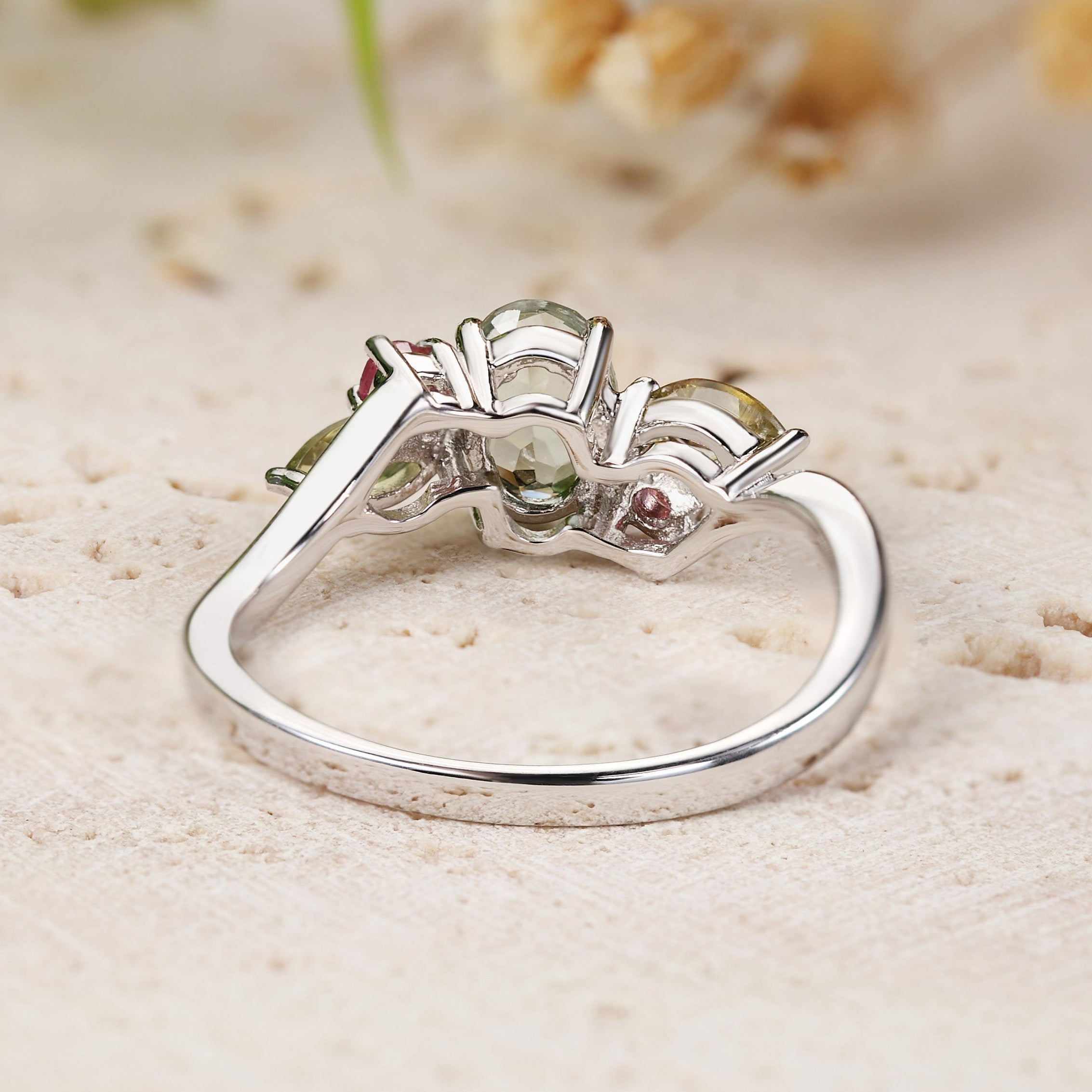 White gold ring with gemstones on a sandy surface with blurred natural background