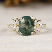 Yellow gold ring with a green gemstone and diamond accents on a light background