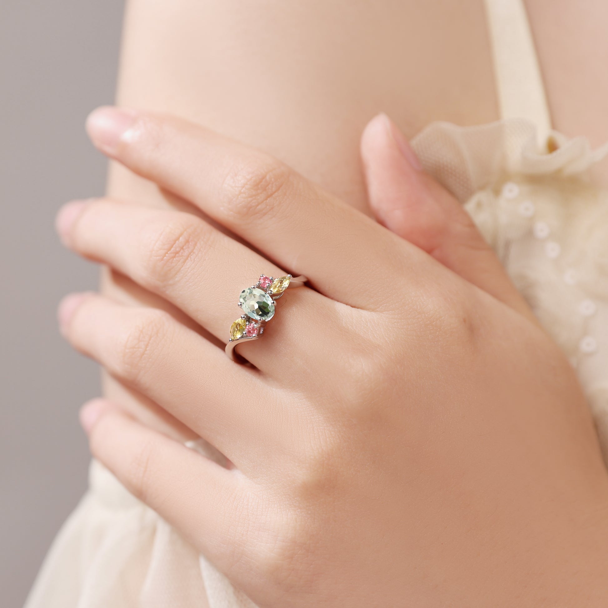 Close-up of a hand wearing a ring with multicolored gemstones on a neutral background