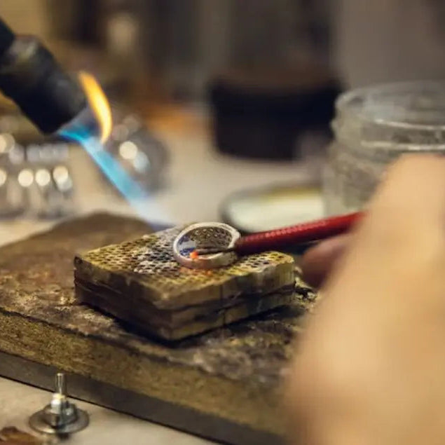 Person working with a torch on a piece of metal, likely jewelry making.