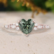 Ring with heart-shaped green gemstone and rose gold setting on a blurred natural background