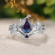 Silver ring with purple gemstone on a light surface with blurred greenery in the background