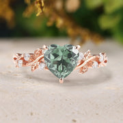 Rose gold ring with a heart-shaped green gemstone on a neutral background