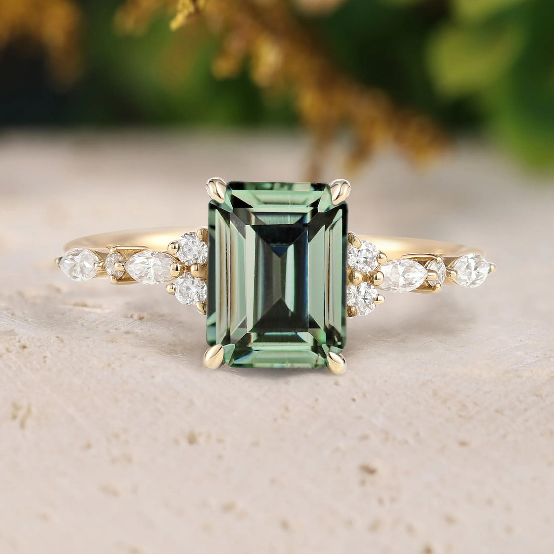 Gold ring with a green gemstone and diamond accents on a textured surface.