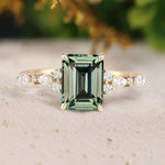 Gold ring with a green gemstone and diamond accents on a textured surface.