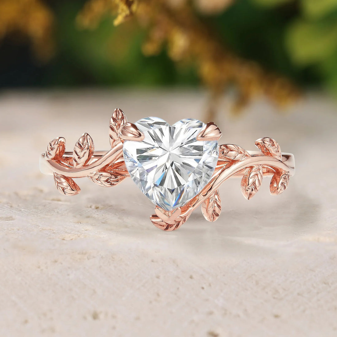 Rose gold ring with heart-shaped diamond on a textured surface with blurred greenery in the background