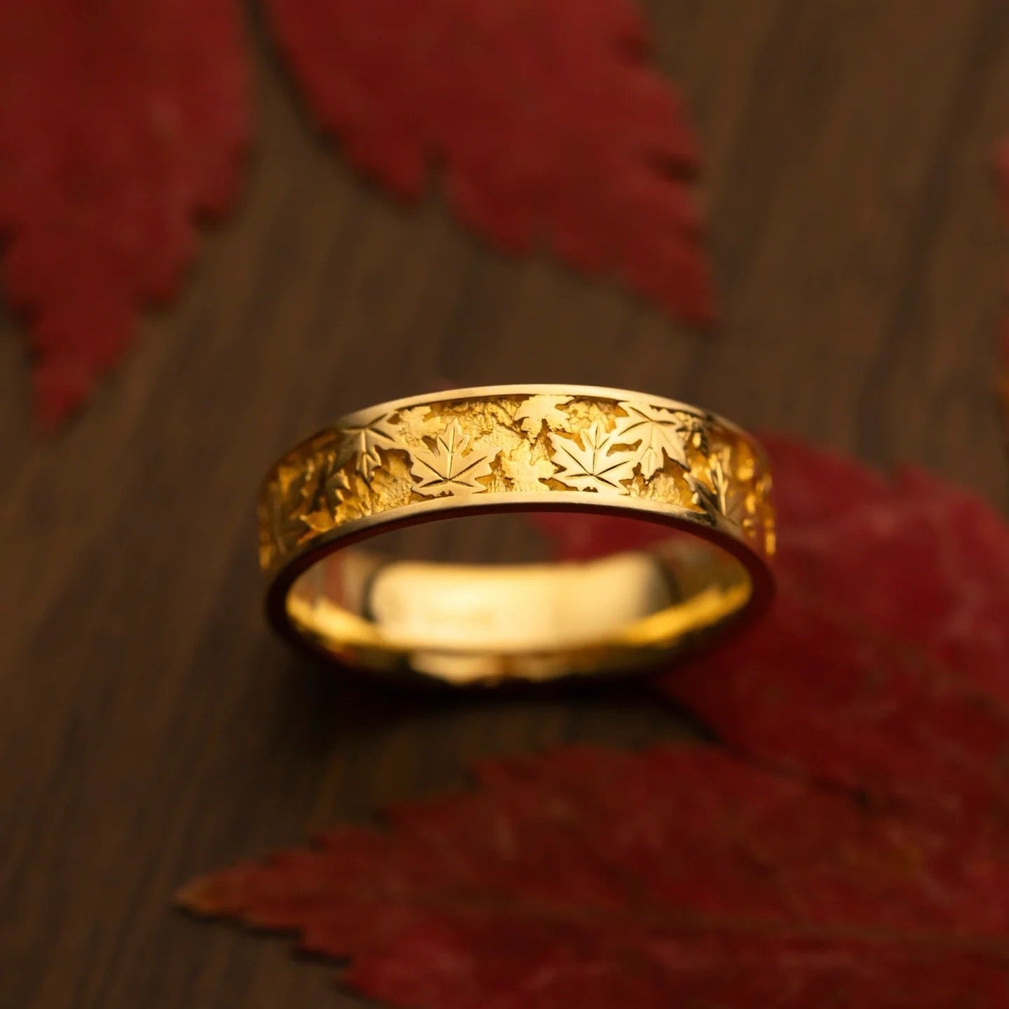 Gold ring with leaf pattern on a wooden surface with red leaves