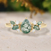 Gold ring with green gemstones and diamonds on a textured surface with blurred natural background