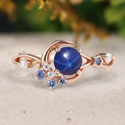 Rose gold ring with a blue gemstone and smaller diamonds on a beige surface.